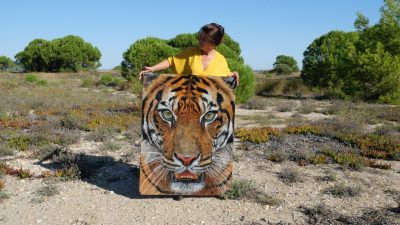 Photo d’Anne Marguet, artiste peintre, posant dans une pinède avec sa toile grand format, "Dans les yeux d’Indrah", un tigre de Sumatra