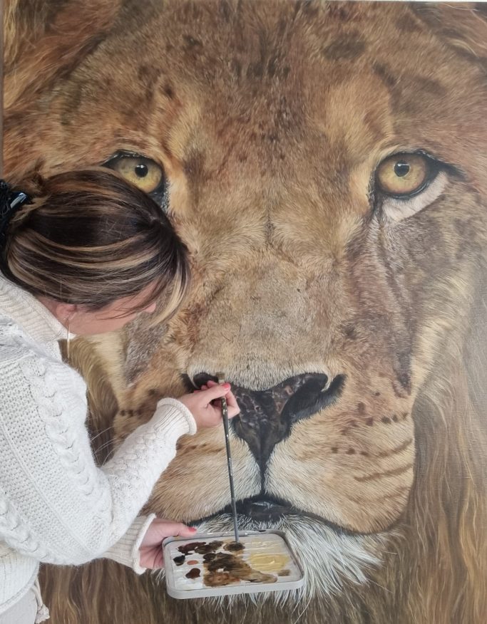 Femme peignant un lion, se concentrant sur les détails du visage de l'animal.